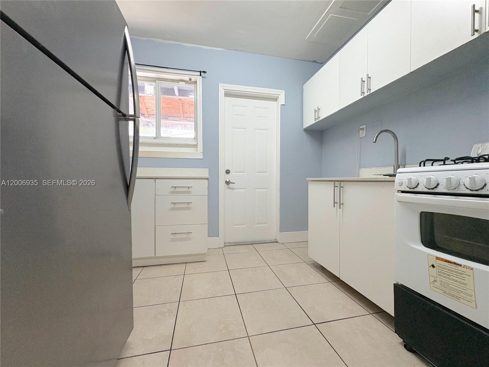 A kitchen features light blue walls, white cabinets, a stove, and light-colored tile flooring — 1815 Mckinley St # 9, Hollywood FL 33020, HOLLYWOOD, FL