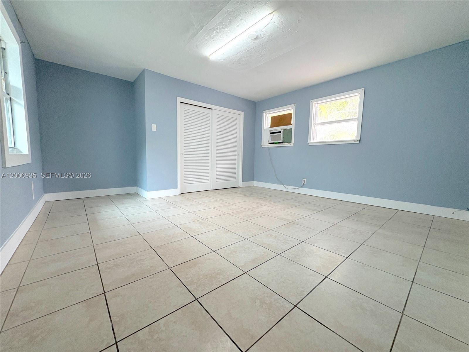 A bedroom features light blue walls, tiled flooring, a closet, and two windows — 1815 Mckinley St # 9, Hollywood FL 33020, HOLLYWOOD, FL