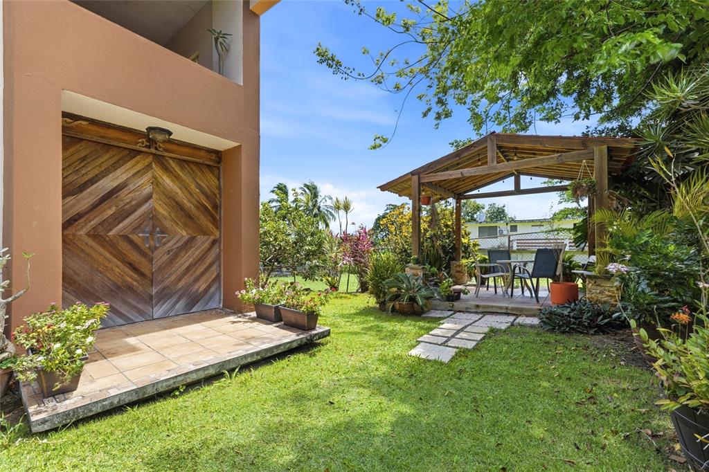 A backyard features a tiled patio, a wooden gazebo, and a large wooden garage door — 10 FORTUNA 27 A, LUQUILLO, PR
