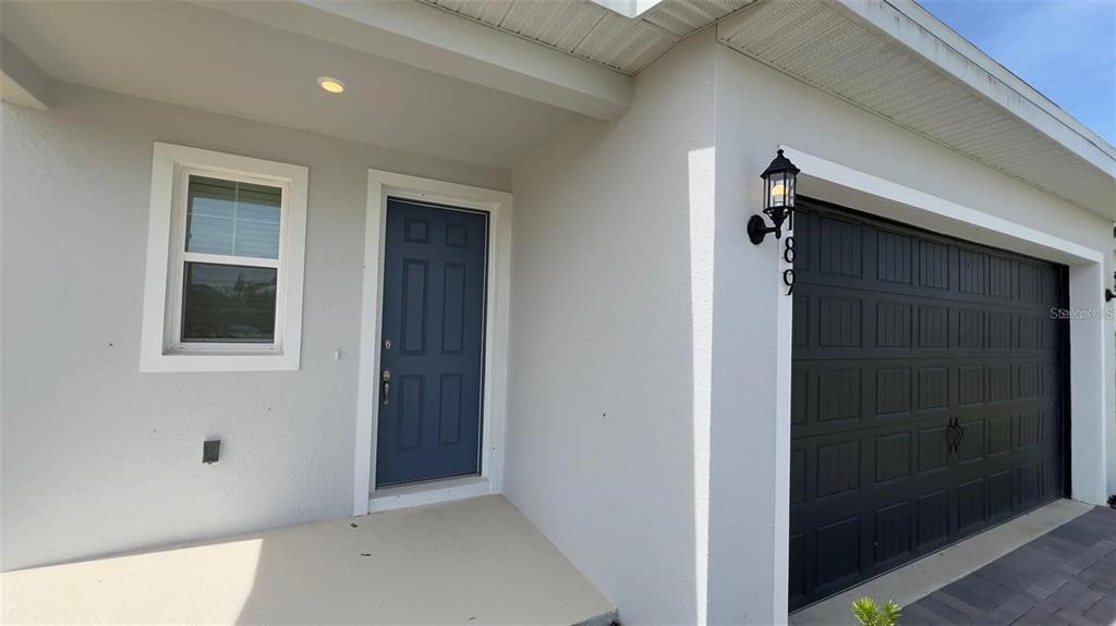 The exterior of a house features a blue front door and a dark garage door — 2189 SUNSHINE PEAK DRIVE, MINNEOLA, FL