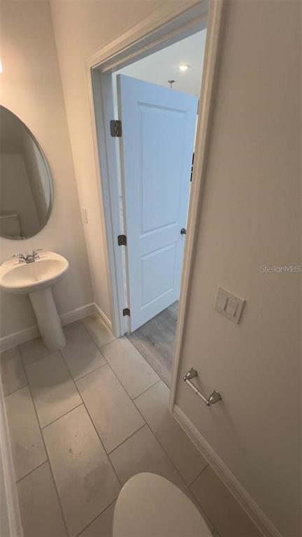 A half bathroom features a pedestal sink, a round mirror, and a door leading elsewhere — 2189 SUNSHINE PEAK DRIVE, MINNEOLA, FL