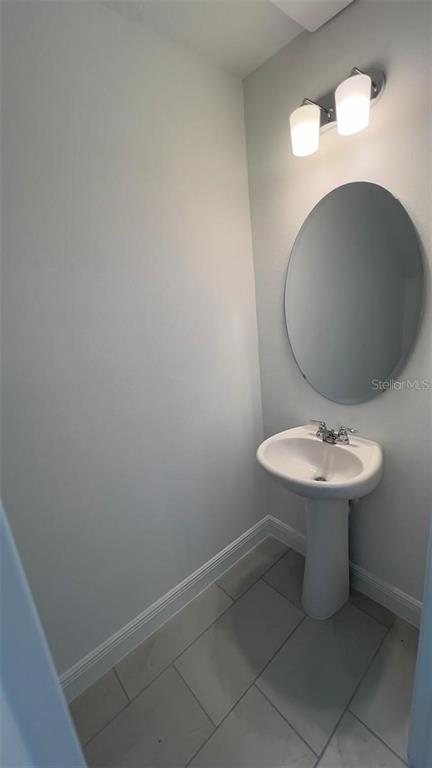 A small bathroom features a pedestal sink, an oval mirror, and a two-light vanity fixture — 2189 SUNSHINE PEAK DRIVE, MINNEOLA, FL