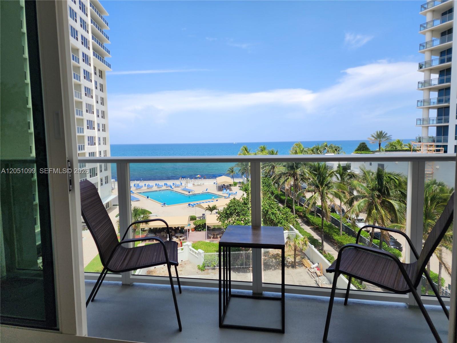 A balcony with two chairs and a table overlooks a swimming pool and the ocean — 3505 S Ocean Dr # 521, Hollywood FL 33019, HOLLYWOOD, FL