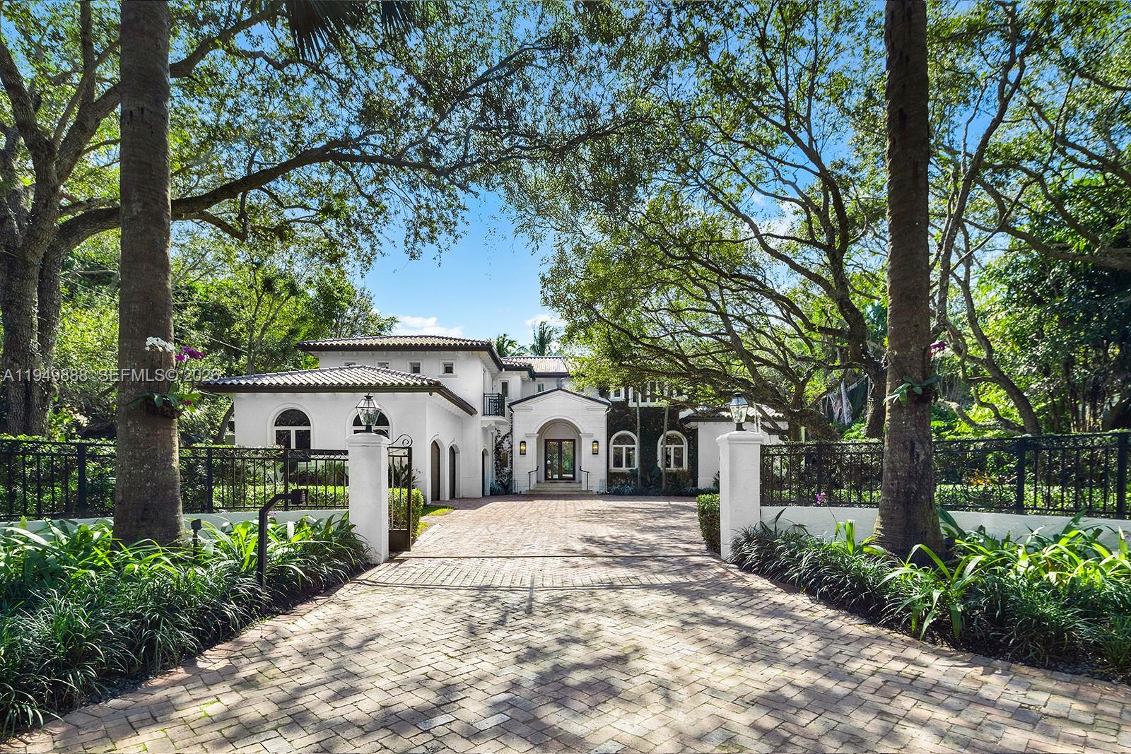 A white two-story Mediterranean-style house sits behind a brick driveway and iron gate — 5002 SW 86th St, Miami FL 33143, MIAMI, FL