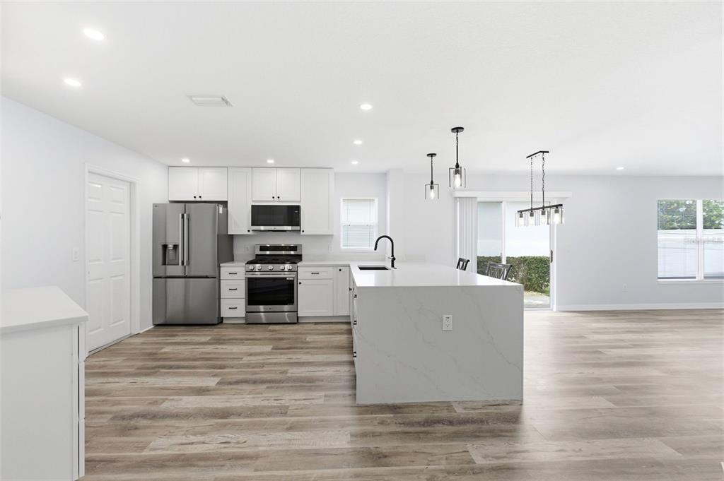 A modern kitchen features white cabinetry, stainless steel appliances, a quartz island, and wood flooring — 1083 JACKSON STREET, THE VILLAGES, FL