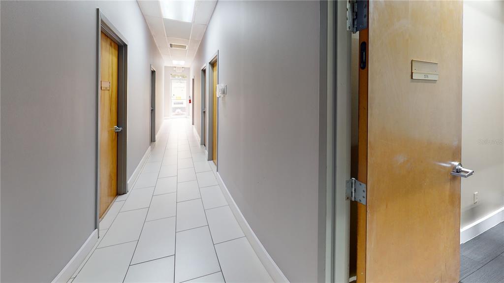 A long office hallway features light gray walls, white tile flooring, and several wooden doors — 1576 TROPIC PARK DRIVE UNIT 1576, SANFORD, FL