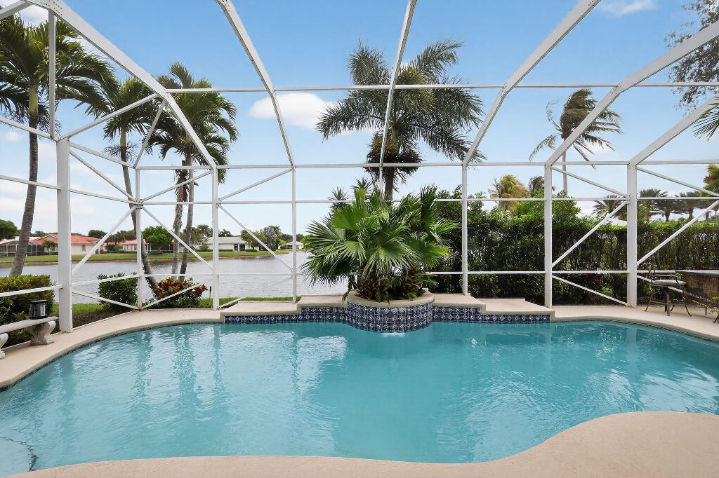 A swimming pool with a tiled planter sits inside a screened-in lanai overlooking a lake — 9430 Lantern Bay Circle, West Palm Beach FL 33411, WEST PALM BEACH, FL