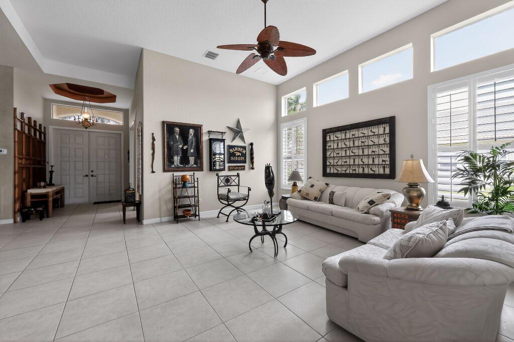 A spacious living room with tile floors, high ceilings, a ceiling fan, and white sofas — 9430 Lantern Bay Circle, West Palm Beach FL 33411, WEST PALM BEACH, FL