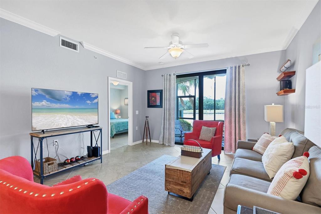 A living room features a grey sofa, two red armchairs, a television, and a sliding door — 17108 VARDON TERRACE UNIT 105, BRADENTON, FL