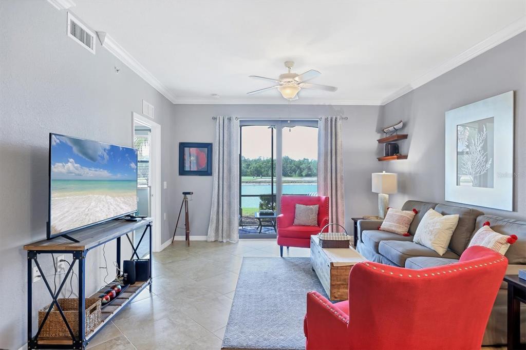 A living room features a grey sofa, two red armchairs, and a view of water — 17108 VARDON TERRACE UNIT 105, BRADENTON, FL