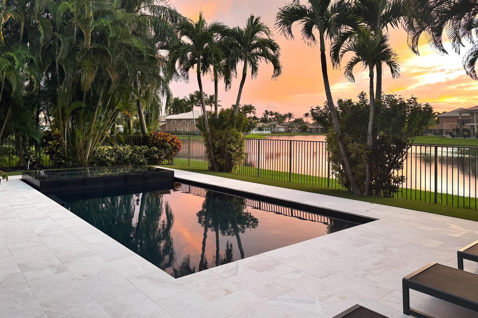 A dark swimming pool with a stone deck overlooks a lake at sunset — 19123 Two River Lane, Boca Raton FL 33498, BOCA RATON, FL