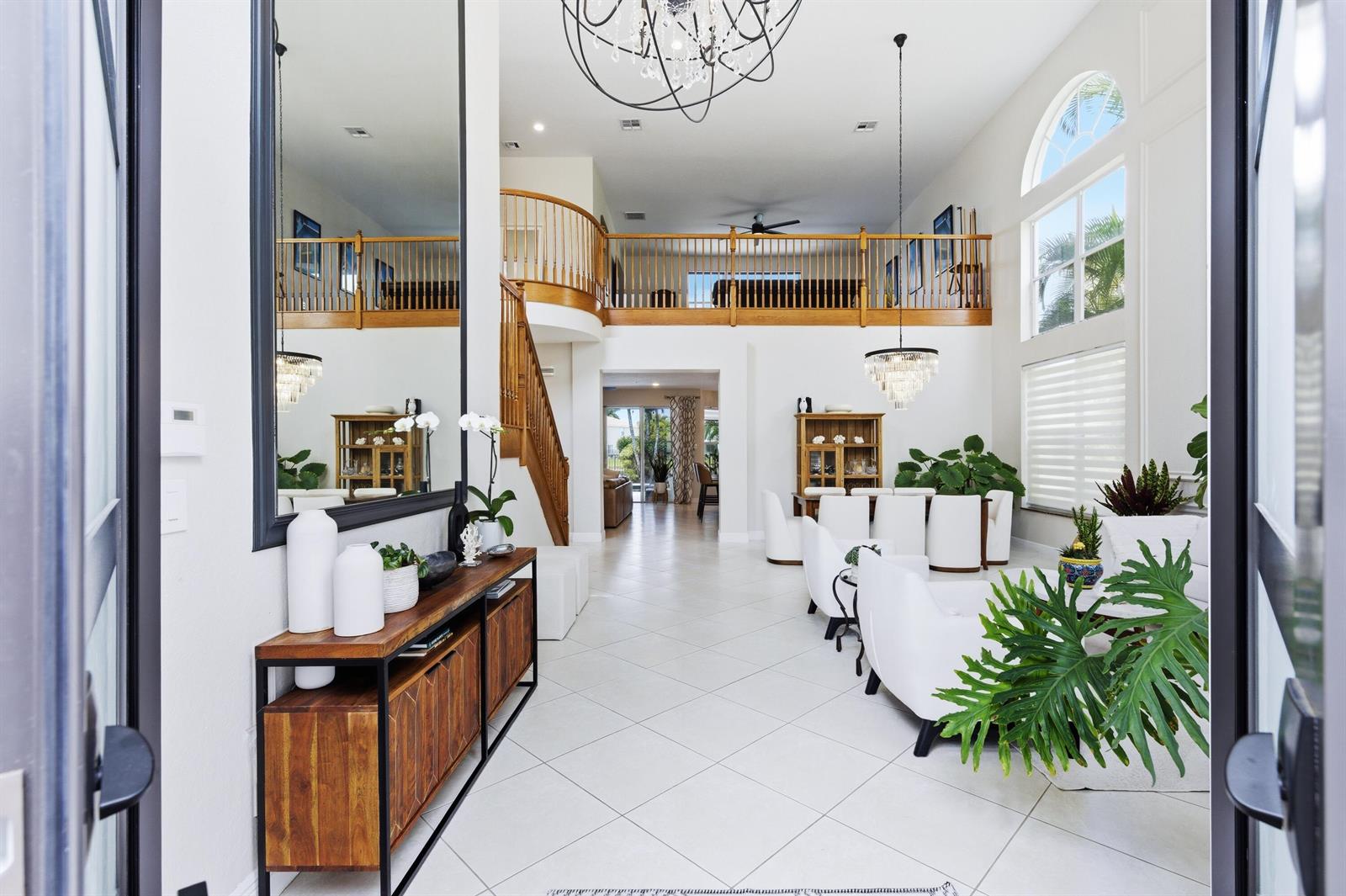A bright, two-story foyer features a wooden console table, a large mirror, and a staircase — 19123 Two River Lane, Boca Raton FL 33498, BOCA RATON, FL