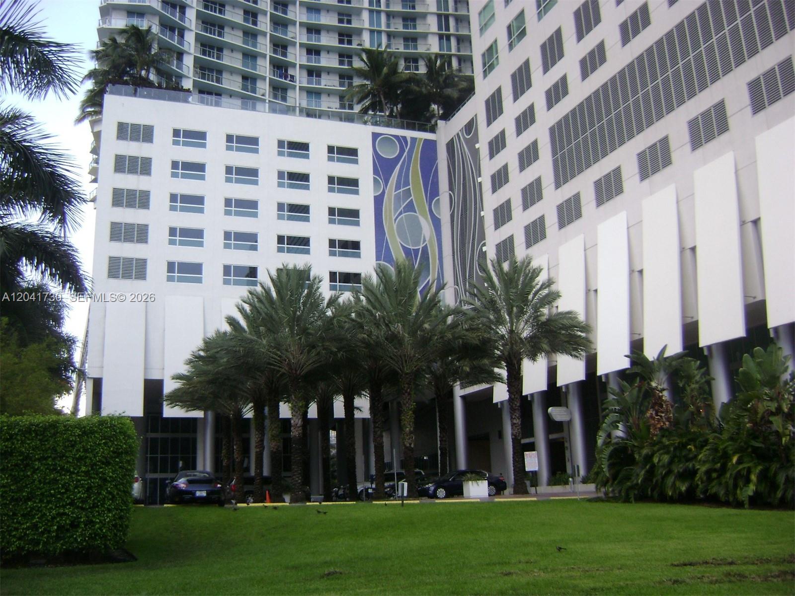 A modern high-rise building exterior features palm trees, a green lawn, and decorative wall panels — 185 SW 7th St # 2104, Miami FL 33130, MIAMI, FL