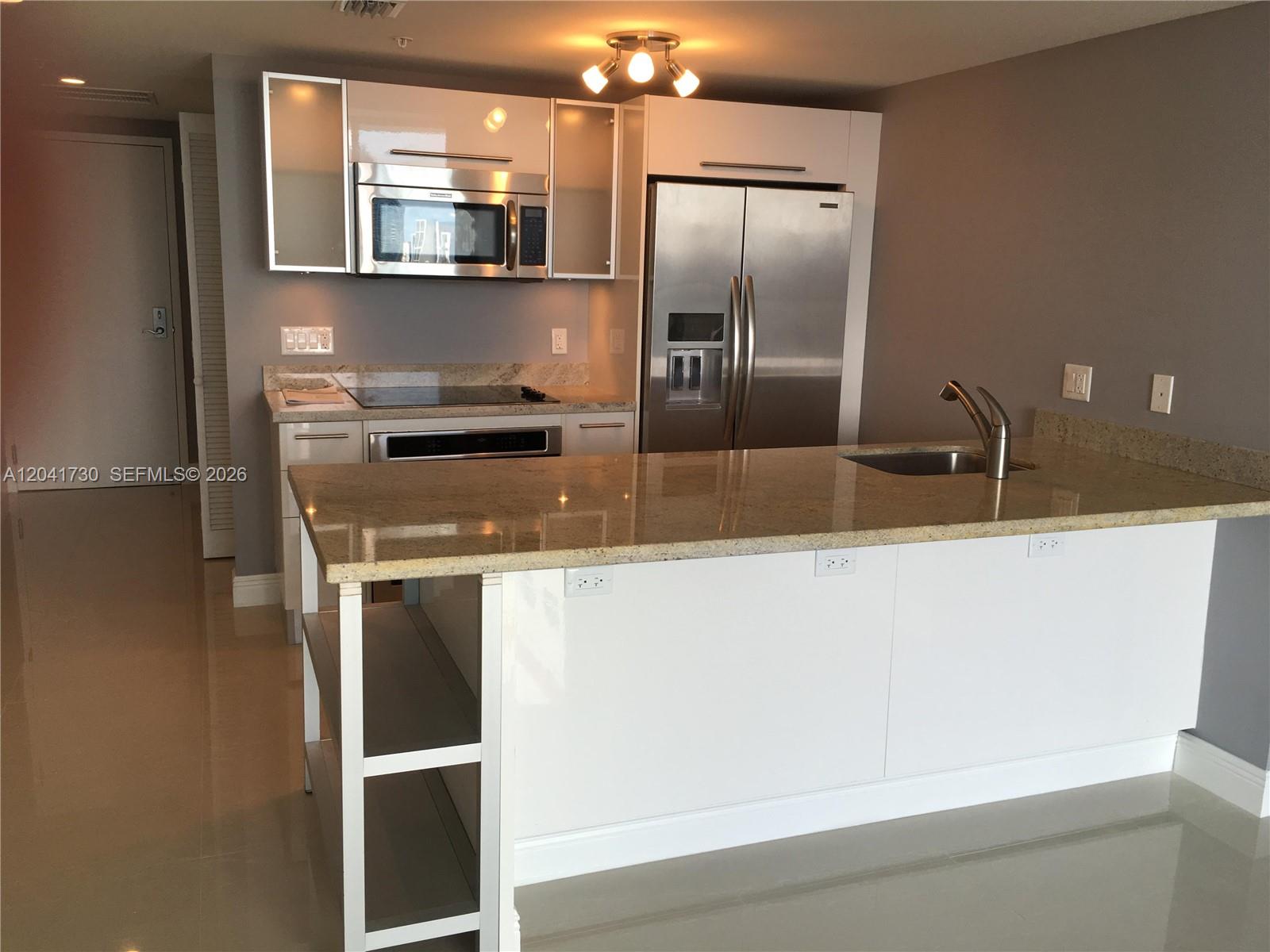 A modern kitchen features white cabinets, stainless steel appliances, and a granite-topped island — 185 SW 7th St # 2104, Miami FL 33130, MIAMI, FL