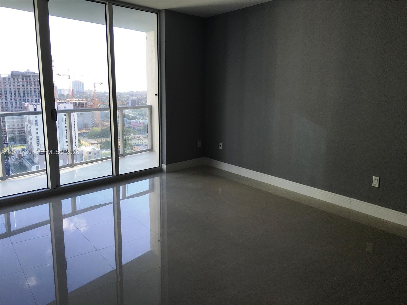 An empty room with gray walls, tile flooring, and a balcony overlooking a city skyline — 185 SW 7th St # 2104, Miami FL 33130, MIAMI, FL