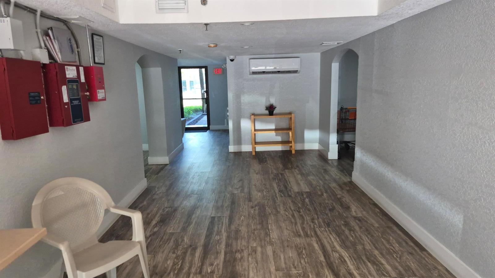 A hallway with wood-look flooring, a white chair, a wooden shelf, and an exit door — 450 Egret Circle # 9510, Delray Beach FL 33444, DELRAY BEACH, FL