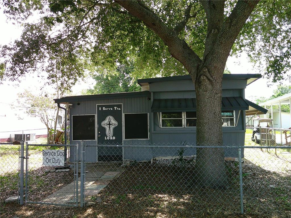 A small gray house with a cross on the door and a chain-link fence — 6250 CONNECTICUT STREET, ZEPHYRHILLS, FL