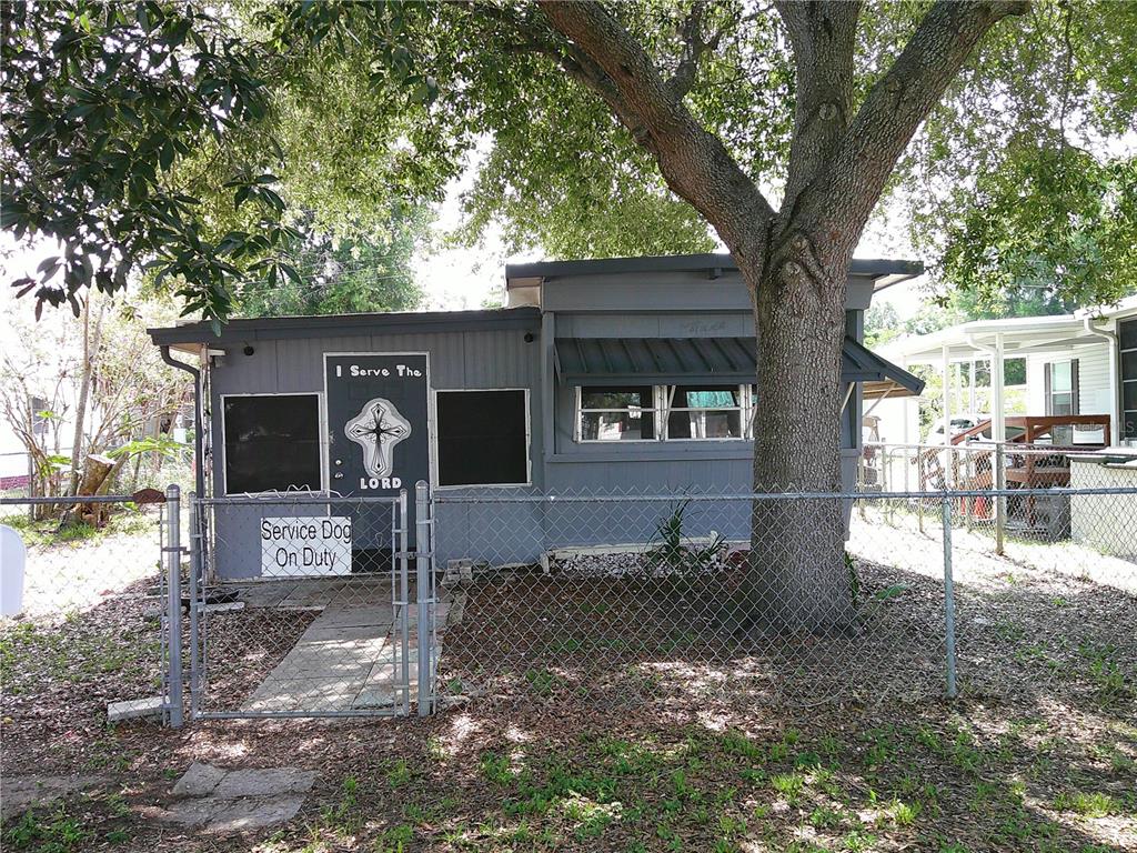 A gray single-story house with a fenced yard, a large tree, and a cross-adorned door — 6250 CONNECTICUT STREET, ZEPHYRHILLS, FL