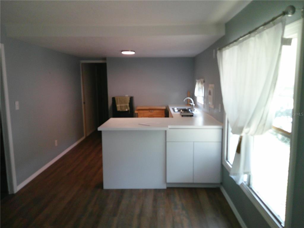 A kitchen with white cabinets and a peninsula counter overlooks a room with wood flooring — 6250 CONNECTICUT STREET, ZEPHYRHILLS, FL