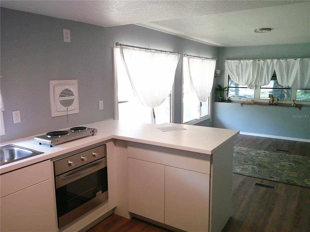 A kitchen with white cabinets, a built-in oven, and a cooktop overlooks a living area — 6250 CONNECTICUT STREET, ZEPHYRHILLS, FL