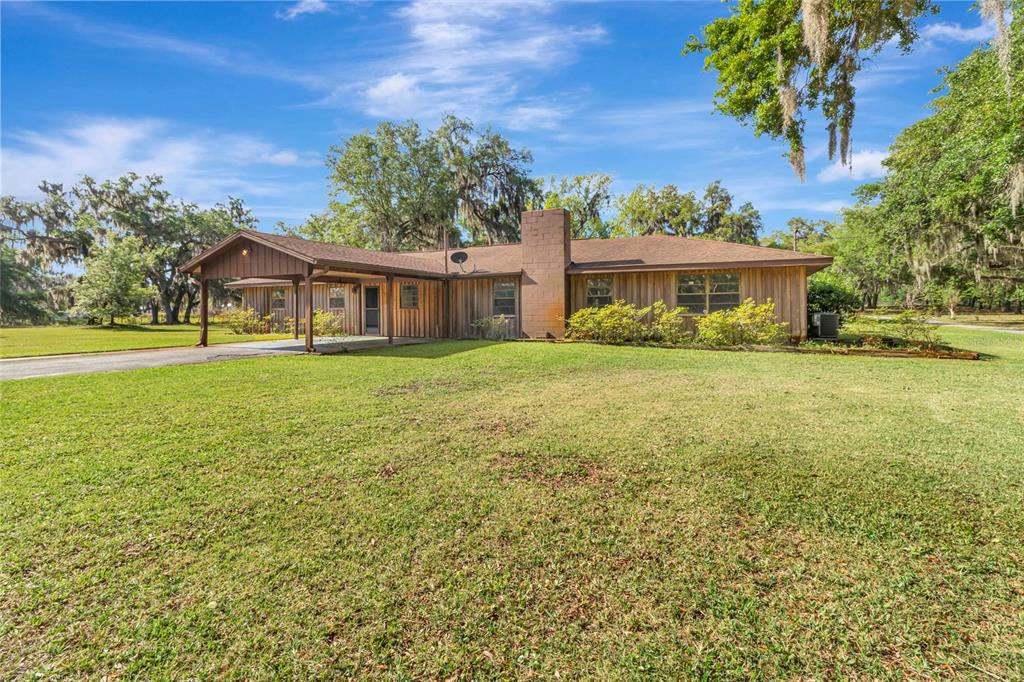A single-story house with wood siding, a brick chimney, and an attached carport — 1520 LEGACY WOODS COURT, GROVELAND, FL