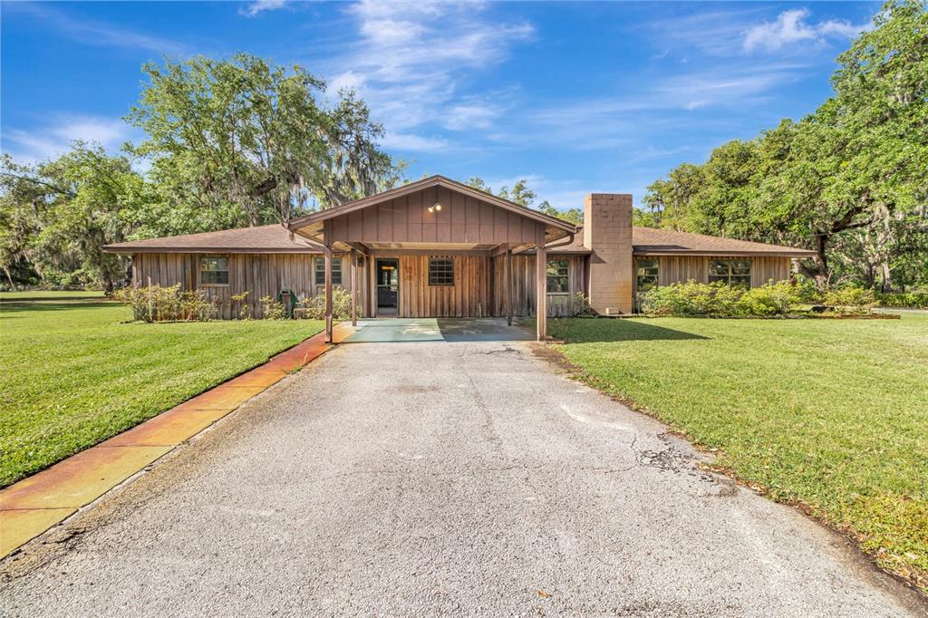 A single-story house with wood siding and a covered carport sits on a grassy lot — 1520 LEGACY WOODS COURT, GROVELAND, FL