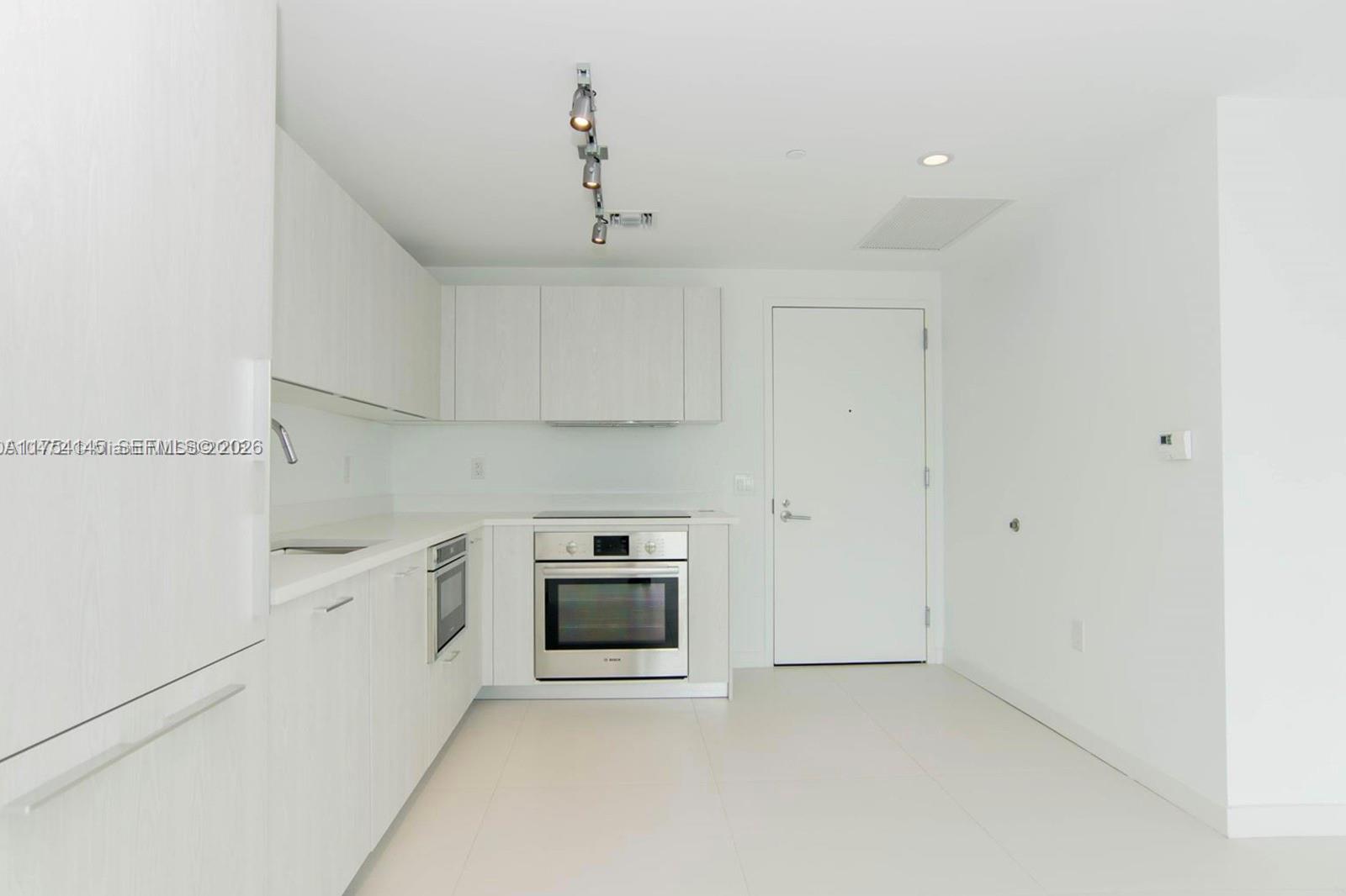 A modern, minimalist kitchen features white cabinetry, stainless steel appliances, and light-colored tile flooring — 501 NE 31st St # 2009, Miami FL 33137, MIAMI, FL