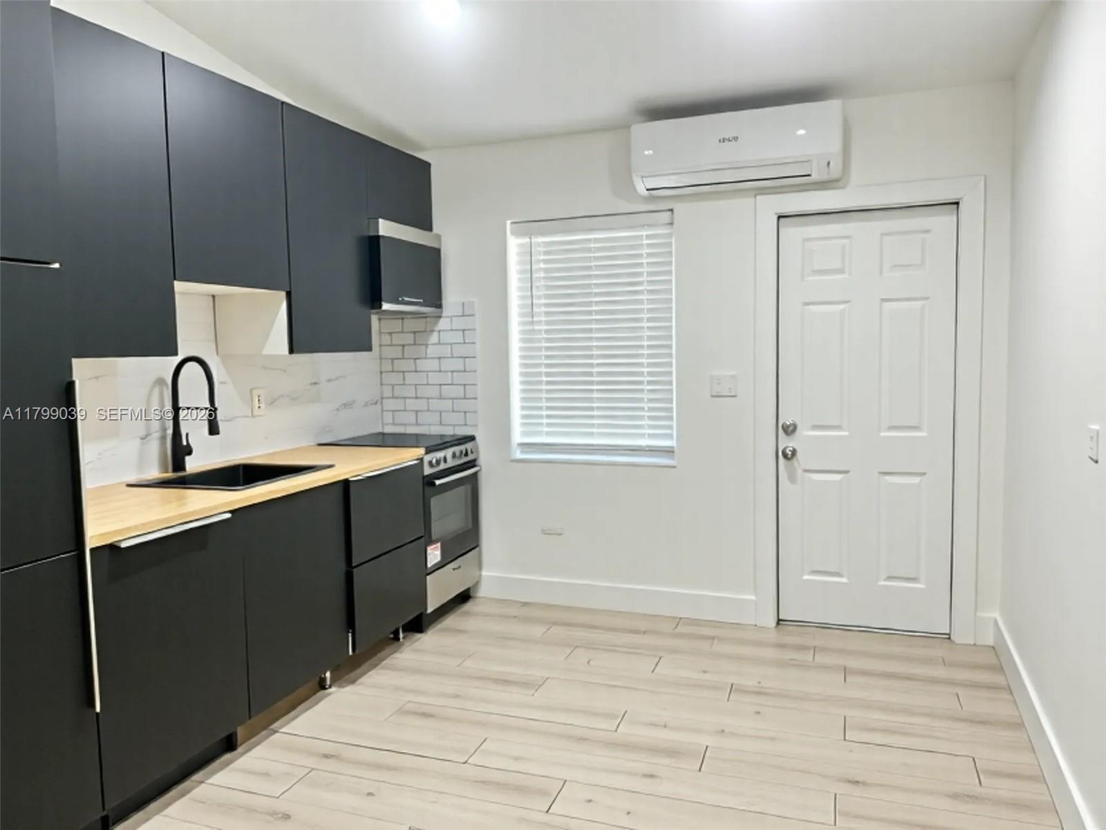 A modern kitchen features black cabinets, light wood countertops, and a white door — 16204 NE 18th Ct, North Miami Beach FL 33162, NORTH MIAMI BEACH, FL