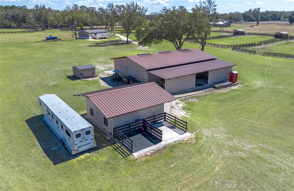 An aerial view shows a metal-roofed barn, a smaller outbuilding, and a horse trailer on a grassy lot — 4700 NW 157TH COURT, MORRISTON, FL