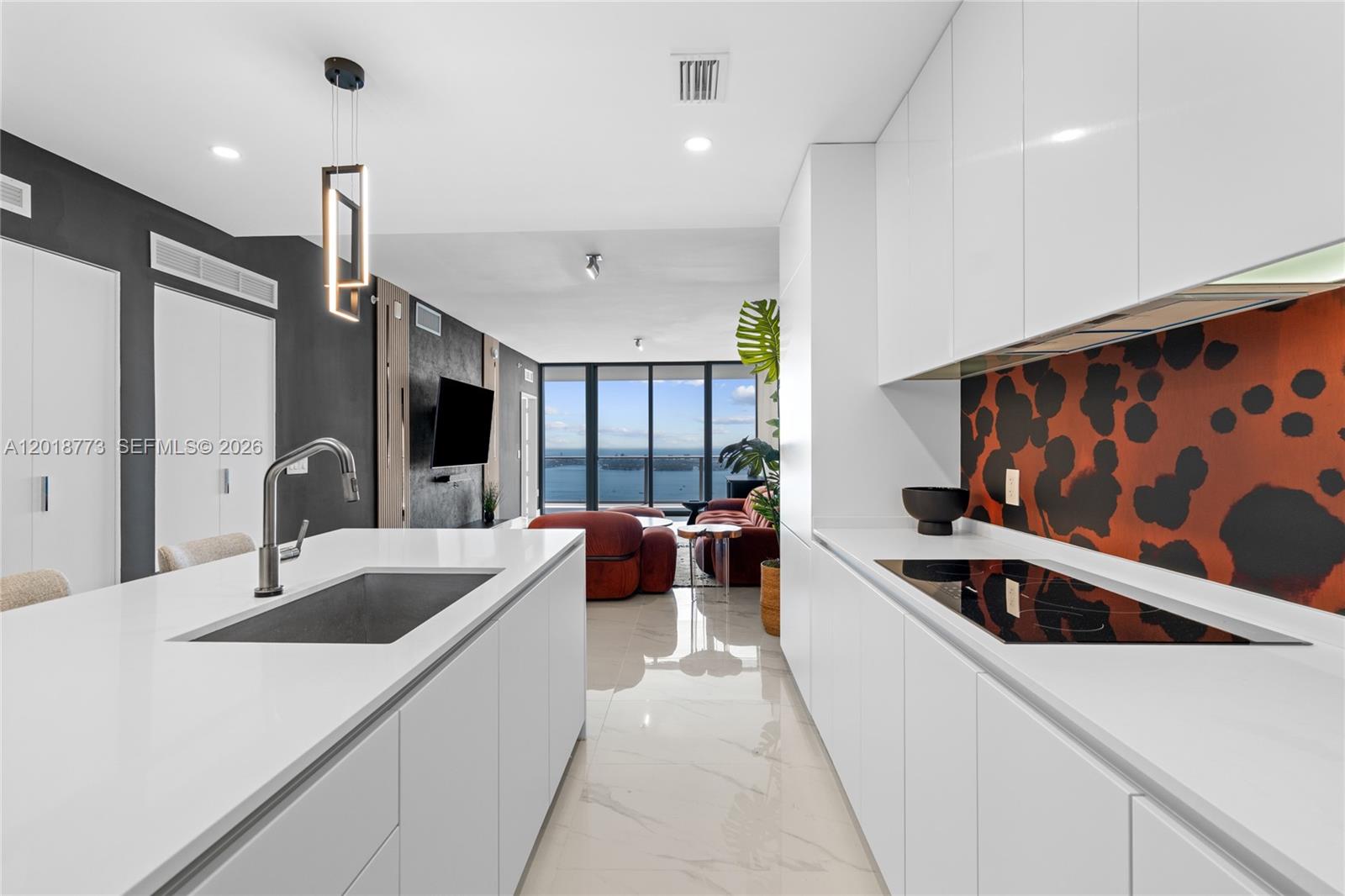 A modern kitchen with white cabinetry and a patterned backsplash overlooks a living area — 700 NE 24th St # 5206, Miami FL 33137, MIAMI, FL