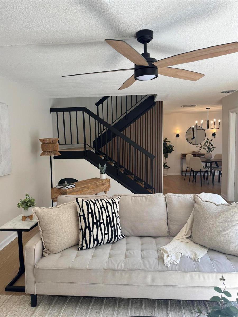 A living room features a beige sofa, a black ceiling fan, and a modern staircase — 6372 Seven Springs Boulevard # A, FL 33463, FL