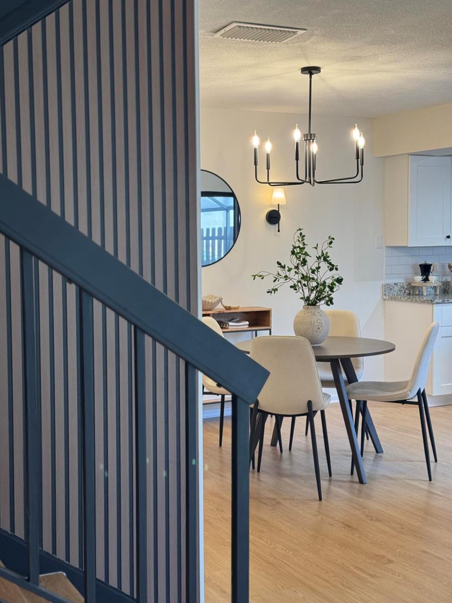 A dining area with a round table and chairs is viewed past a slatted staircase railing — 6372 Seven Springs Boulevard # A, FL 33463, FL
