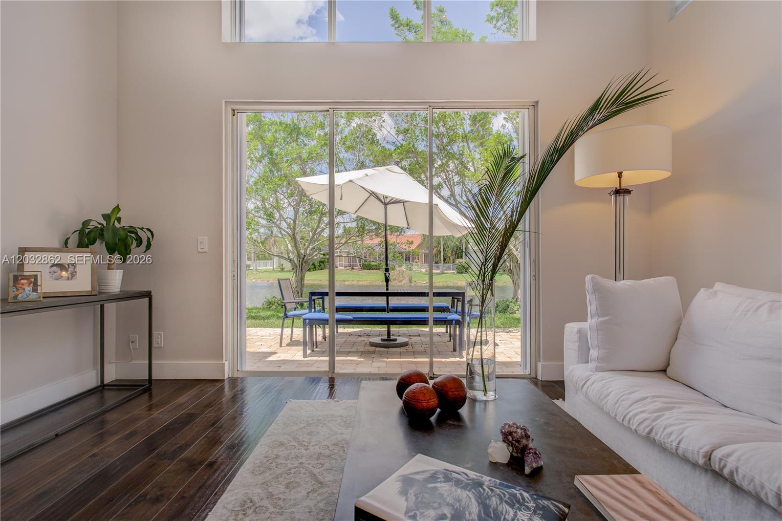A living room with dark wood floors opens to a patio with a lake view — WESTON, FL
