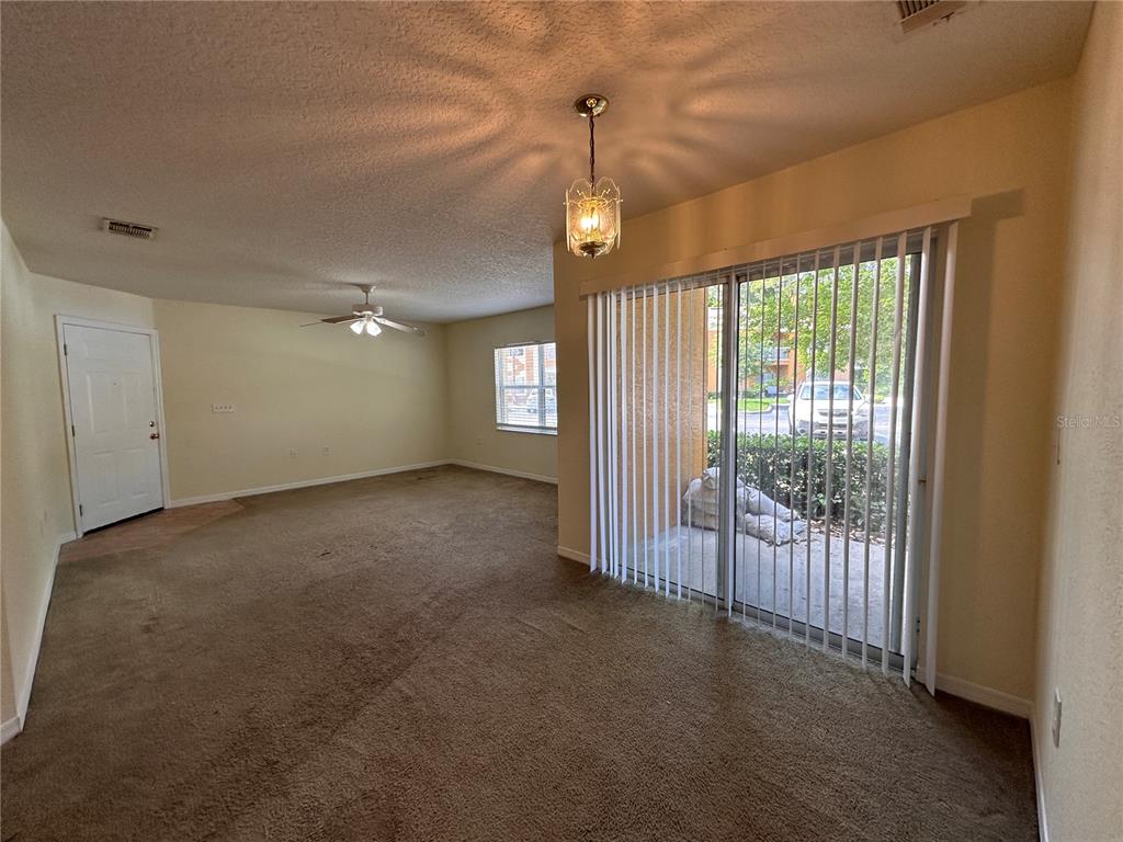An empty living room features brown carpeting, a ceiling fan, a chandelier, and sliding glass doors — 4600 E MOODY BOULEVARD UNIT 12B, BUNNELL, FL