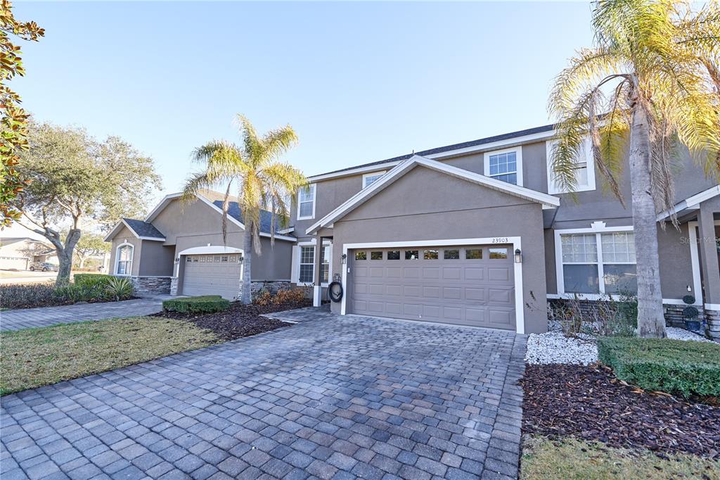 A two-story suburban house with a paved driveway, two garages, and palm trees — 23903 SARDINIA DRIVE, SORRENTO, FL