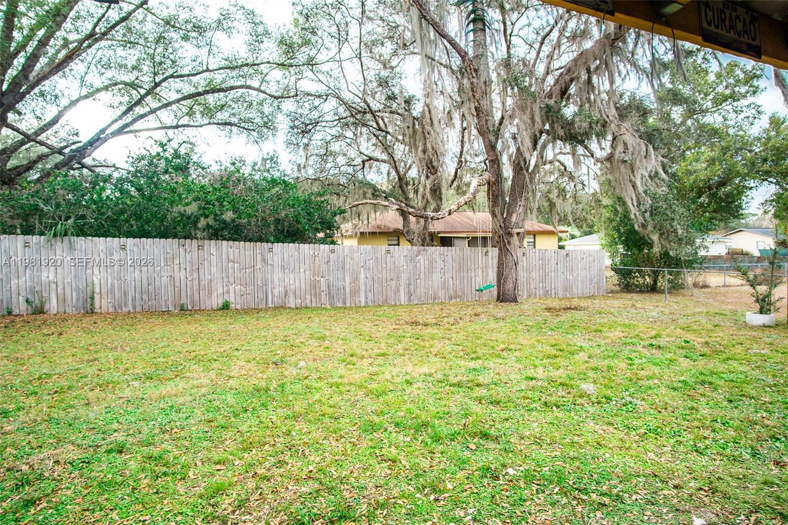 A grassy backyard features a wooden fence, large trees with Spanish moss, and a swing — 1123 Bucknell, Inverness FL 34450, INVERNESS, FL
