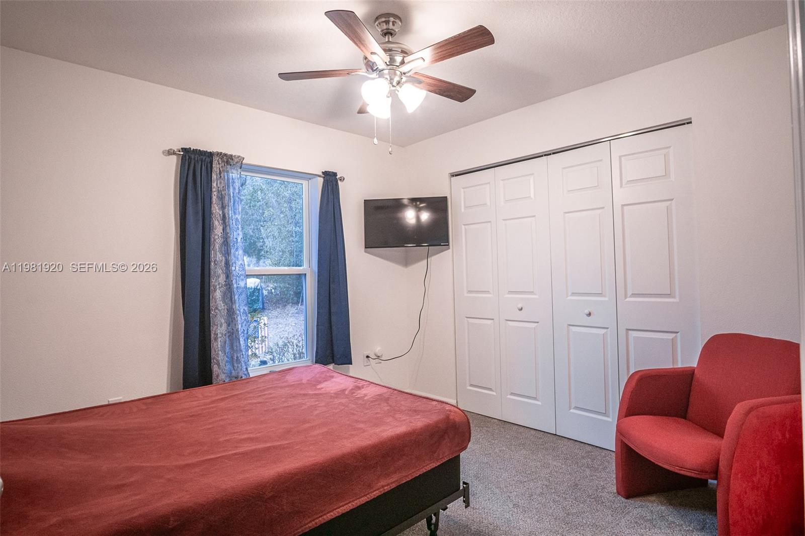 A bedroom features a bed with a red cover, a red chair, and a ceiling fan — 1123 Bucknell, Inverness FL 34450, INVERNESS, FL