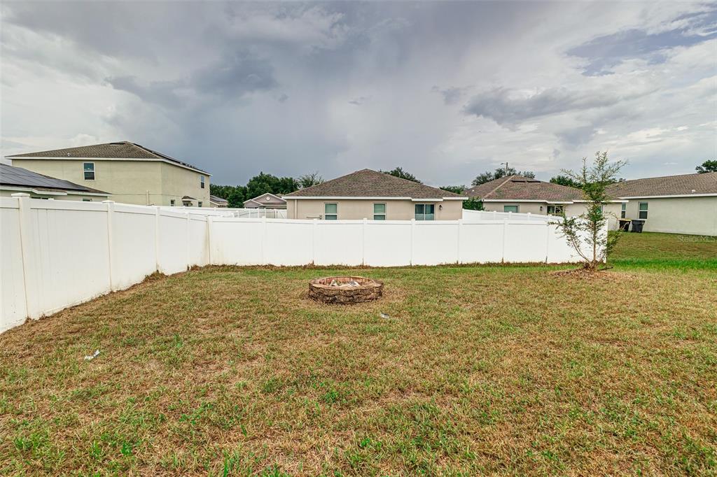 A backyard features a stone fire pit, a white vinyl fence, and surrounding residential homes — 538 PATTON LOOP, BARTOW, FL