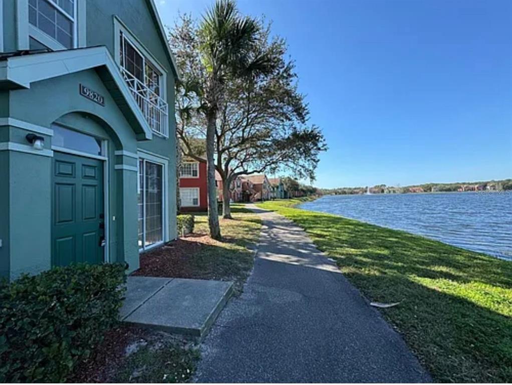 A teal multi-story building sits beside a paved walkway and a large lake — 9820 LAKE CHASE ISLAND WAY UNIT 9820, TAMPA, FL