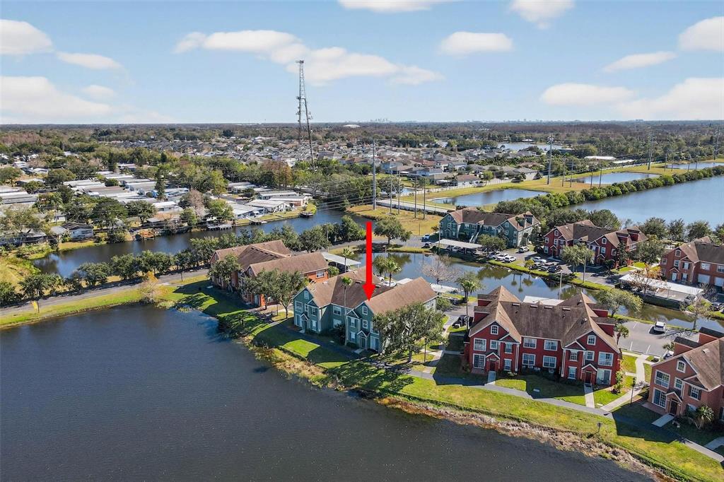 An aerial view shows multi-story apartment buildings situated along a lake in a residential area — 9820 LAKE CHASE ISLAND WAY UNIT 9820, TAMPA, FL