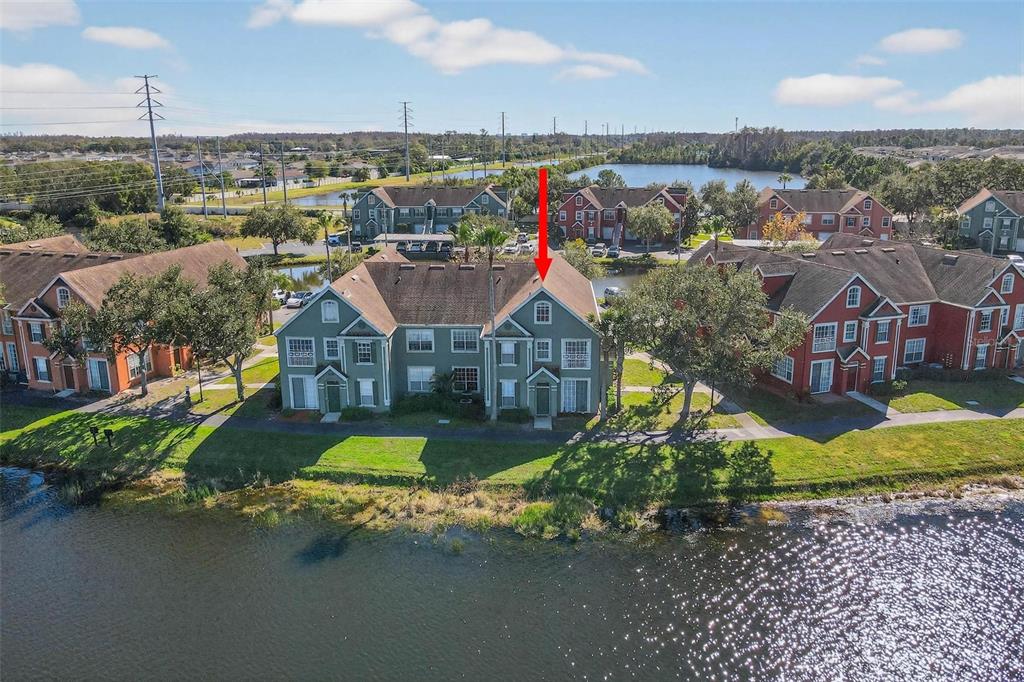 An aerial view shows a multi-story green apartment building situated along a waterfront — 9820 LAKE CHASE ISLAND WAY UNIT 9820, TAMPA, FL