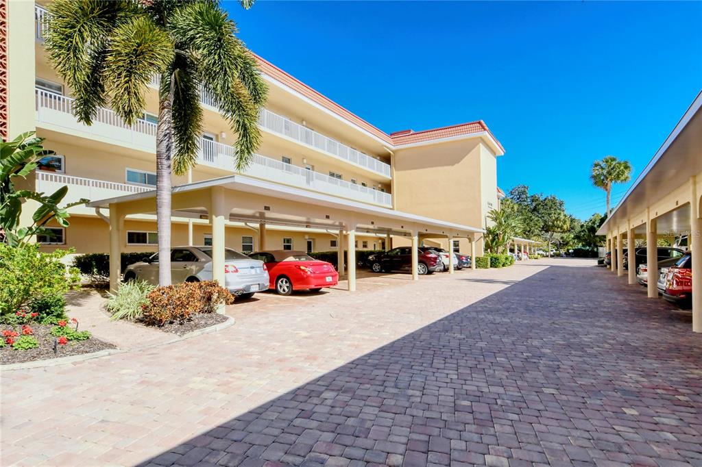 A paved parking area with covered spaces sits beneath a multi-story apartment building — 1257 S PORTOFINO DRIVE UNIT 38ALBA, SARASOTA, FL