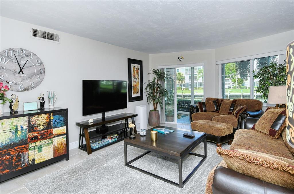 A living room features a large wall clock, a television on a stand, and brown furniture — 1257 S PORTOFINO DRIVE UNIT 38ALBA, SARASOTA, FL