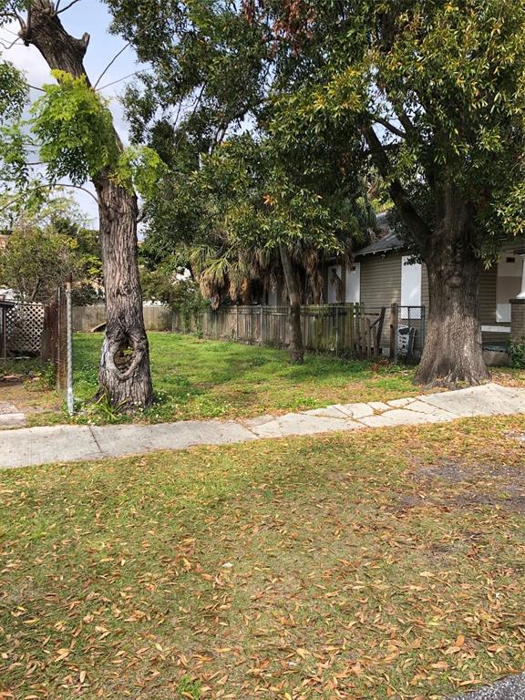 A vacant, grassy lot sits between two large trees next to a boarded-up house — 2515 W UNION STREET, TAMPA, FL