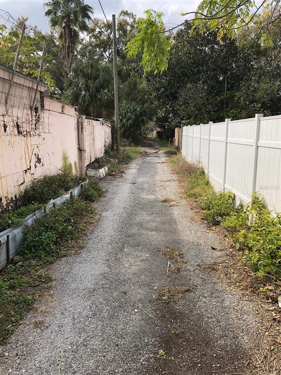 A narrow gravel alleyway runs between a weathered pink wall and a white vinyl fence — 2515 W UNION STREET, TAMPA, FL