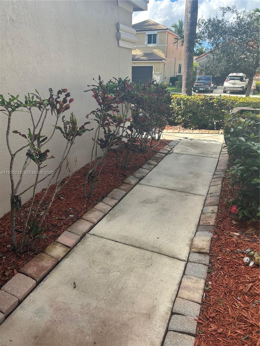 A concrete walkway lined with brick pavers runs alongside a house with landscaped shrubs — 948 NW Phoenix Way, Weston FL 33327, WESTON, FL