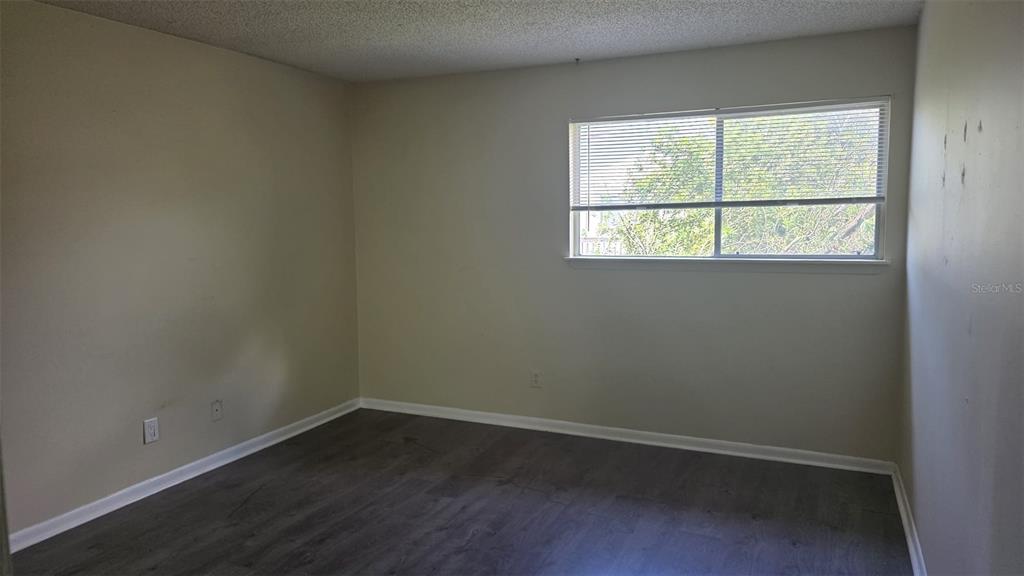 An empty bedroom features beige walls, dark wood-look flooring, and a window with blinds — 6328 NEWTOWN CIRCLE UNIT B2, TAMPA, FL
