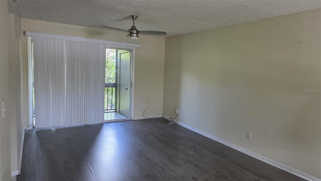 An empty living room features dark wood-look flooring, a ceiling fan, and a sliding glass door — 6328 NEWTOWN CIRCLE UNIT B2, TAMPA, FL