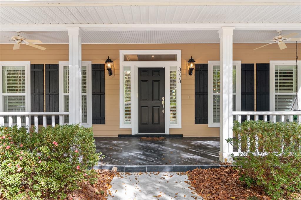A front porch with a black door, dark tiled flooring, and white columns — 3773 SW 21ST DRIVE, GAINESVILLE, FL