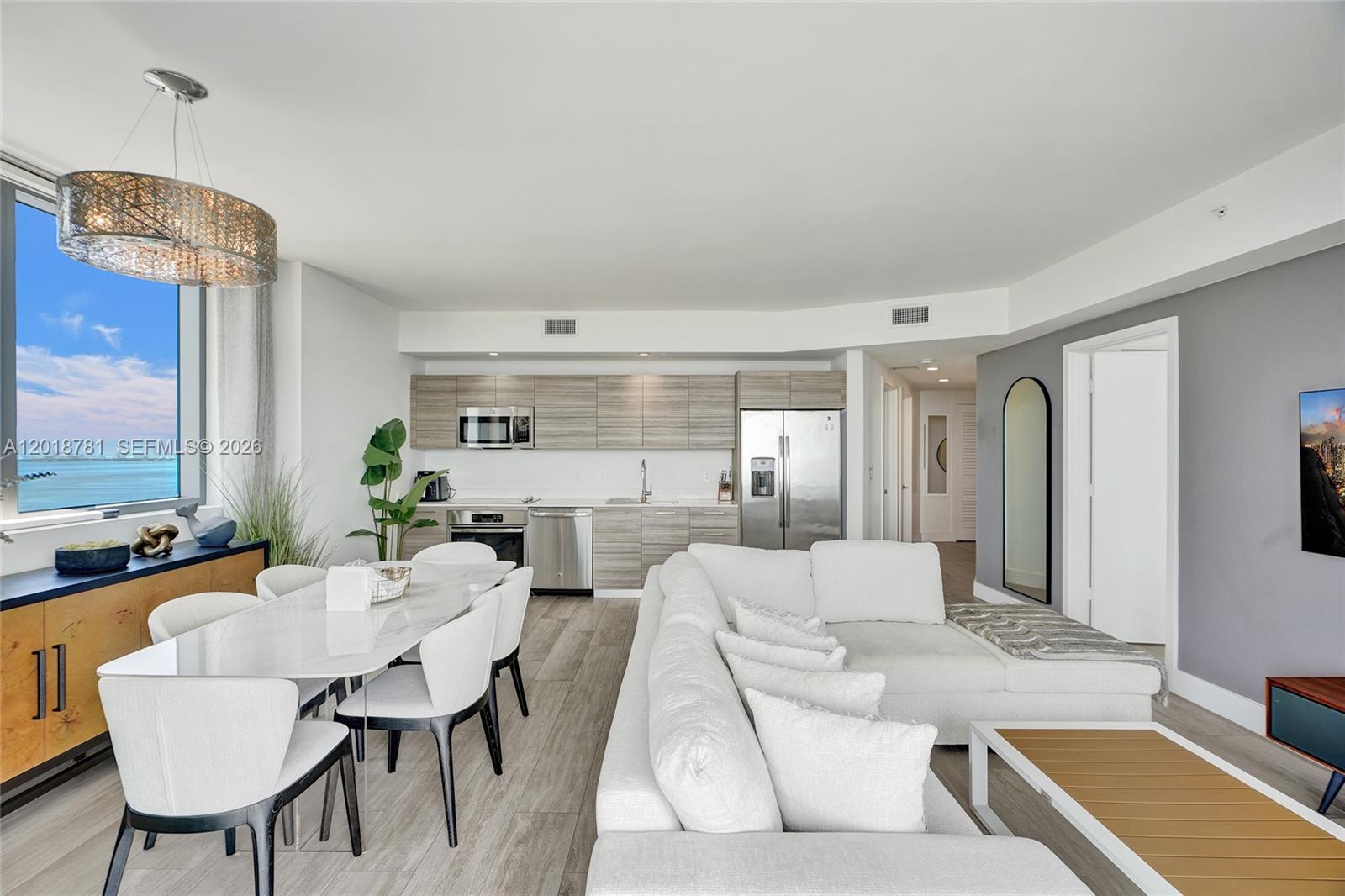 An open-concept living and dining area features a modern kitchen, white sofa, and ocean view — 121 NE 34th St # 2809, Miami FL 33137, MIAMI, FL